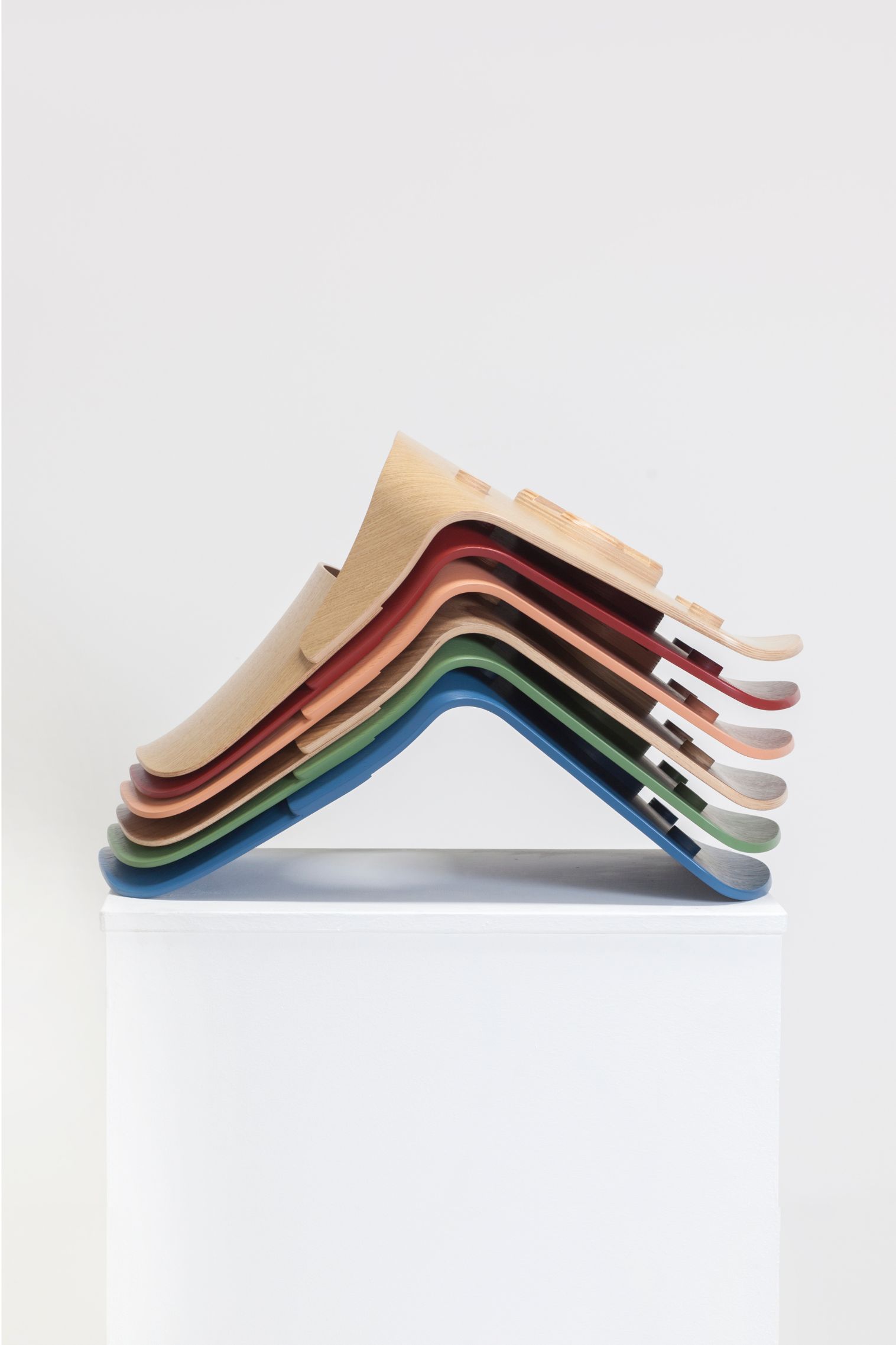 Colourful molded plywood chair shells packed in an aesthetic way on a white peddestal